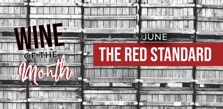Background is a wide shot of our stacked grape bins. In the left foreground,text includes "Wine of the Month." The right foreground text states "June The Red Standard."